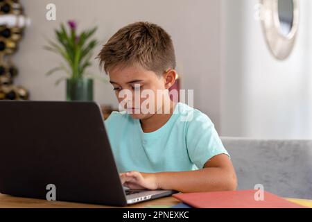 Cute caucasian focused boy doing homework over laptop on table while sitting at home, copy space Stock Photo