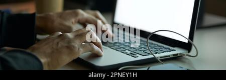 Close up shot of hands of man sitting at the table in front of computer monitor and using laptop while working late at night Stock Photo