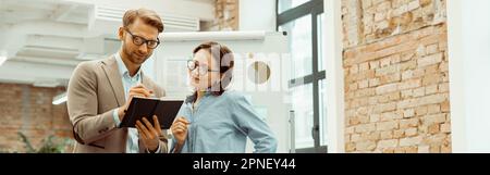 Smiling two colleagues looking at notepad in the office Stock Photo