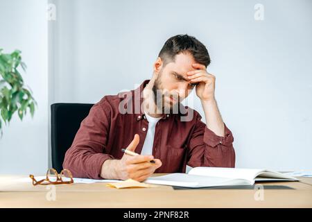 Frustrated upset tired caucasian man, company manager, tired of working with documents, feeling stressed, headache, exhausted, not invested in deadlines, nervous, worried, needs a break Stock Photo