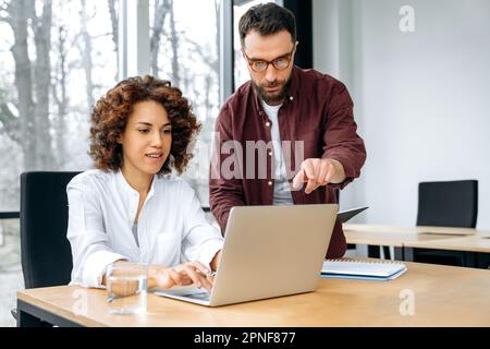 Two successful coworkers of different nationalities, a man and a woman, works together in the office, discuss business goals, ideas for new project, planning business strategy. Collaboration concept Stock Photo