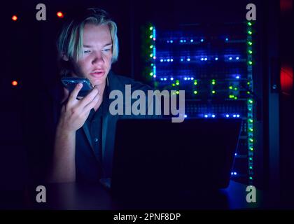 Technician using laptop and smart phone in server room Stock Photo
