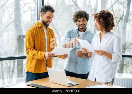 Successful multiracial business partners gathered in meeting room, confident businesspeople discuss new project, creative ideas, promotion strategy, analyze financial risks and profits, smile Stock Photo
