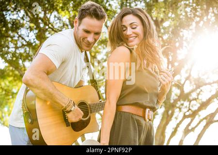 Woman dancing to music while man playing guitar in park Stock Photo