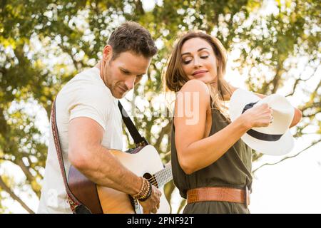 Man playing guitar and woman dancing in park Stock Photo