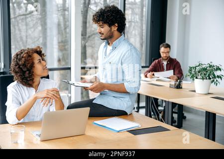 Two coworkers, african american woman and caucasian man, successful colleagues, work together on a project in modern office, brainstorming, work with clients, solve problems, analyzing financial risks Stock Photo