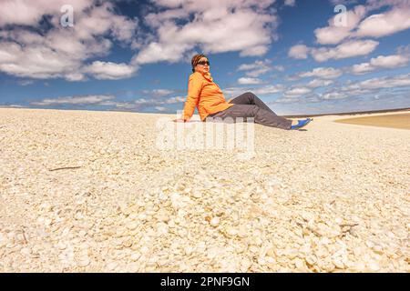 A woman sitting relaxed on pile of sea shell at Shell Beach in Shark Bay region of Western Australia, Australia. Stock Photo