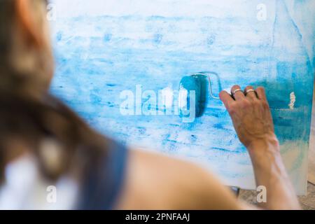 Close up of a woman painting on a canvas a blue abstract painting. Stock Photo