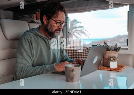 Man sitting in mobile home and working on laptop Stock Photo