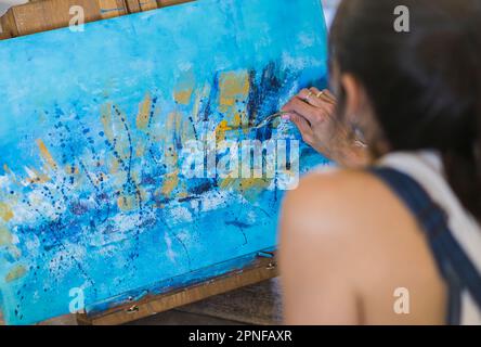 Close up of a woman painting on a canvas a blue abstract painting. Stock Photo