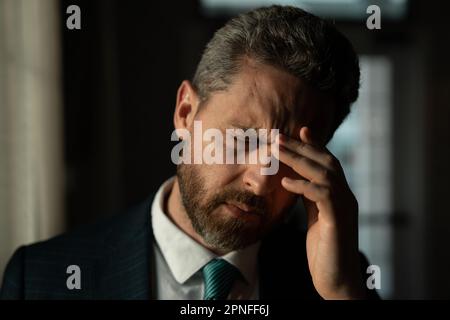 Tired man suffering from headache after computer work, exhausted with closed eyes touching head, relieving pain, migraine. Business problems. Bankrupt Stock Photo