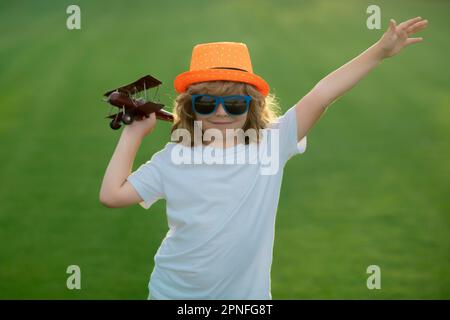 Kid having fun with toy airplane in field. Child pilot aviator with airplane dreams of traveling in summer in nature Stock Photo