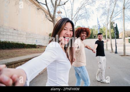 Point view portrait of a multiracial group of friends walking holding hands. pov of young people having fun running hand in hand. First person perspective of three happy teenagers enjoying. friendship. High quality photo Stock Photo