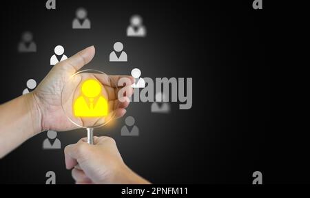 A hand with a magnifying glass and the other hand holding a found potential personnel icon among many others. HRM or Human Resource Management. Human Stock Photo