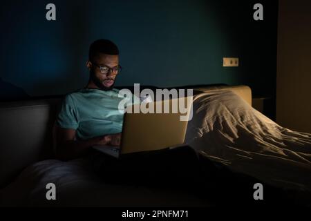 Black guy freelance IT developer using laptop at night, coding until late hours to meet deadline Stock Photo