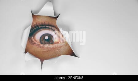 Eye peeking through peep hole watching something scary. Scared woman with look of horror in her eyes looking peeping from a dark room at night Stock Photo