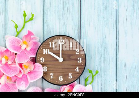 Alarm clock and pink streaked orchid flower on blue wooden background. Stock Photo