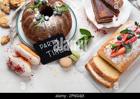Dessert table with various of bundt cakes, pieces of cakes, sweets, cookies with fruit toppings on a white background. Top view. Stock Photo