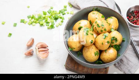 Young boiled potatoes on the plate with parsley and onion on the board. White background. Top view. Panorama. Stock Photo