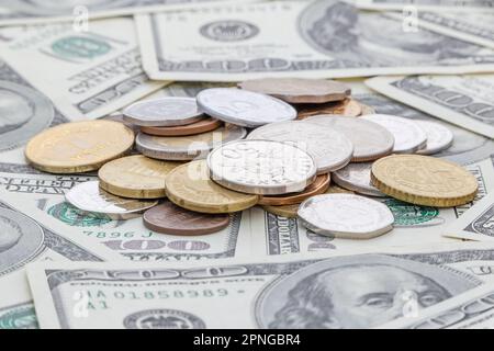 heap of different countries coins lying on one hundred US dollars banknotes Stock Photo