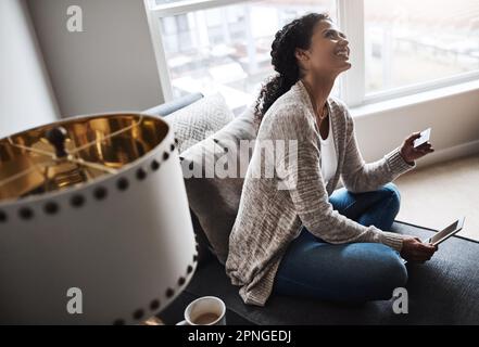 Banking made very simple. a cheerful young woman relaxing on a chair while doing online shopping on a digital tablet at home. Stock Photo