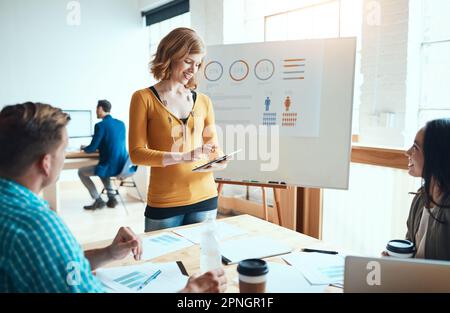 Wireless tech promotes interactive collaborations. a young businesswoman using a digital during a meeting with her colleagues in a modern office. Stock Photo