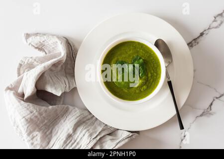 Healthy breakfasts, green broccoli and spinach cream soup in a white bowl on a marble background with a gray napkin, top view Stock Photo