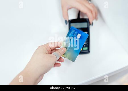 Close up of female hand of the client makes contactless payment with bank card. Another womans hand holds payment terminal. White background. Using el Stock Photo