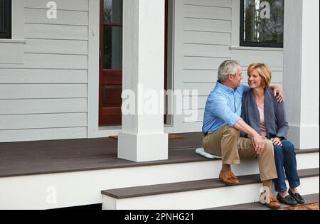 Happiness is having a place to call home. a happy mature couple sitting on the doorstep of their home. Stock Photo