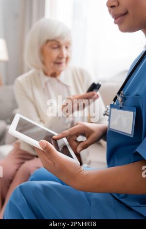 multiracial nurse using digital tablet with blank screen near senior woman on blurred background Stock Photo
