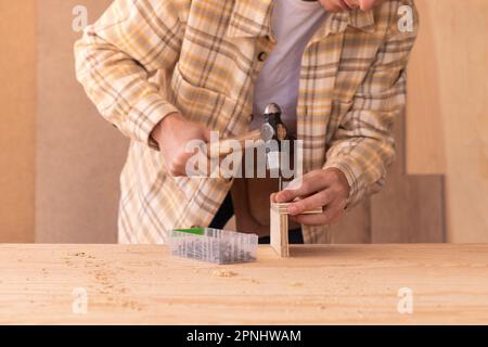 Crop male master in checkered shirt using hammer while connecting wooden details with nail Stock Photo