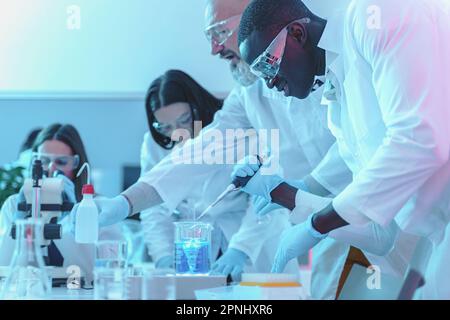 Diverse group of scientists wearing lab coats and safety goggles, working with laboratory equipment such as microscope, test tubes, and pipette. Stock Photo