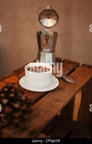A vertical shot of a cup of fresh coffee with a mocha pot on the table with a blurry background Stock Photo