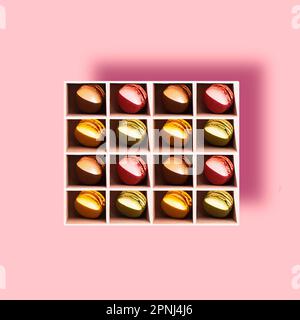 Colourful French macaroon, a sweet meringue-based confection, placed in a box on a colourful background with pieces of fresh berries: strawberries, gr Stock Photo