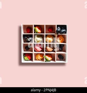 Colourful French macaroon, a sweet meringue-based confection, placed in a box on a colourful background with pieces of fresh berries: strawberries, gr Stock Photo