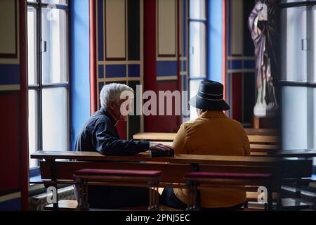 Rear view of senior priest talking to visitor while they sitting on bench during ministration in church Stock Photo