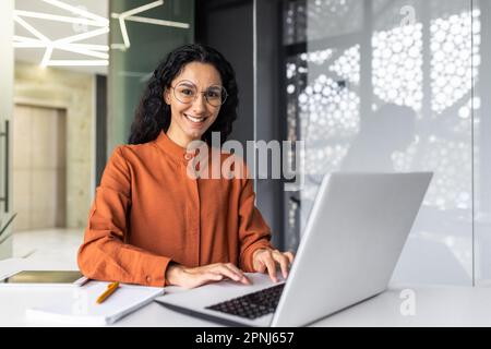 Young beautiful hispanic woman working inside modern office, businesswoman smiling and looking at camera at work using laptop Stock Photo