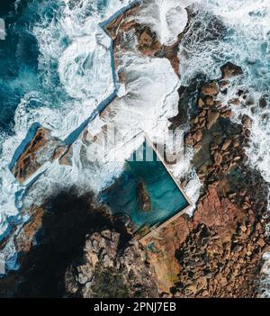 Aerial view early morning light with ocean waves flowing over rocks around North Curl Curl ocean rock pool during storm. Stock Photo