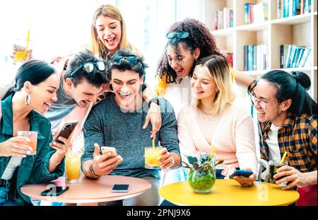 Trendy friends watching viral video on mobile phone at cocktail bar - Young people having fun together on happy hour time - Life style concept with di Stock Photo