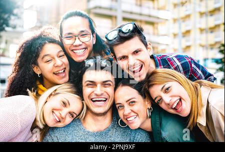 Multi ethnic guys and girls taking selfie out side with backlight - Trendy life style friendship concept on young multiracial best friends having fun Stock Photo