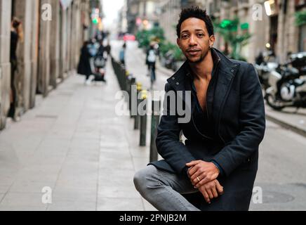 Confident stylish black man looking at camera while posing sitting outdoors in the street. Stock Photo