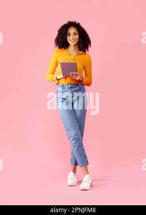 Happy black lady holding digital tablet, using modern gadget for online shopping or distance learning, vertical shot Stock Photo