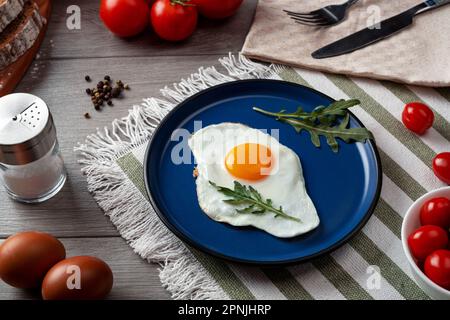 Fried eggs for breakfast. Healthy breakfast with vegetables and herbs. Fried egg on a blue plate. Serving on the table Stock Photo