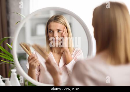 Shocked Middle Aged Woman Looking At Brush Full Of Her Fallen Hair Stock Photo