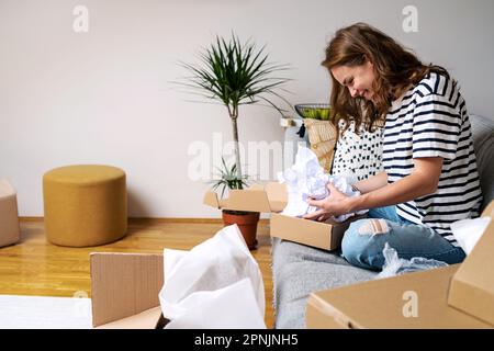 Curly woman unboxing postal parcel with online purchase. Stock Photo
