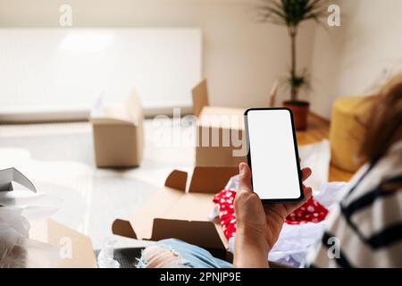 Mockup image of smartphone with blank screen in the hand of woman on the background of opened cardboard boxes. Stock Photo