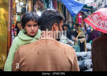 April 19, 2023, Srinagar, Jammu and Kashmir, India: Kashmiri man carrying his child arrive for shopping during a rainfall ahead of the Muslim festival Eid-al-Fitr at a local market in Srinagar. Markets across the Muslim world witness huge shopping rush in preparation for Eid al-Fitr, a celebration that marks the end of the Muslim fasting month of Ramadan. (Credit Image: © Faisal Bashir/SOPA Images via ZUMA Press Wire) EDITORIAL USAGE ONLY! Not for Commercial USAGE! Stock Photo