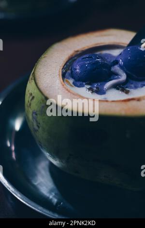 Close-up of popular Filipino dessert shaved ice sundae AKA Halo-halo in coconut or buko shell with two scoops of ube ice cream on top. Selected focus. Stock Photo