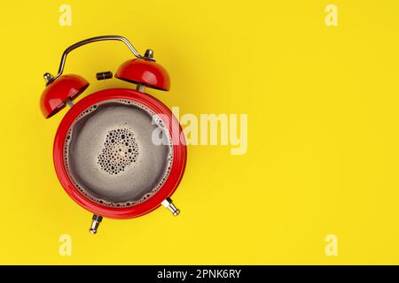 An invigorating morning coffee alarm clock on a yellow background. Coffee in the alarm clock top view. Space for text. Stock Photo