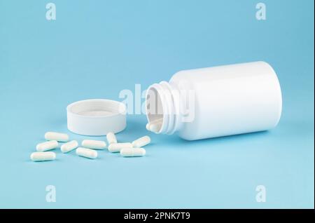 Different drugs and health supplement pills poured from a medicine white bottle health care and medical top view on colored blue background. Stock Photo